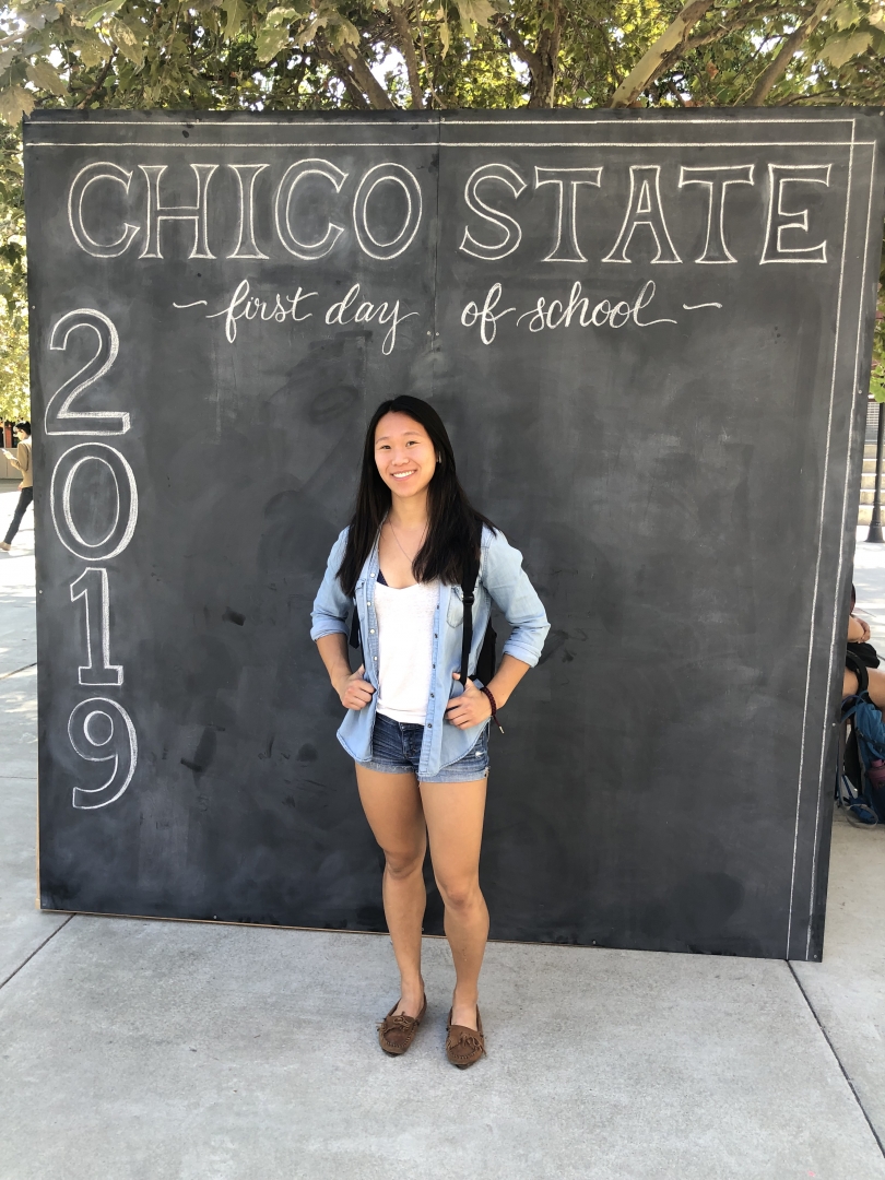 Amy Bell stands in front of a sign that says "Chico State first day of school."