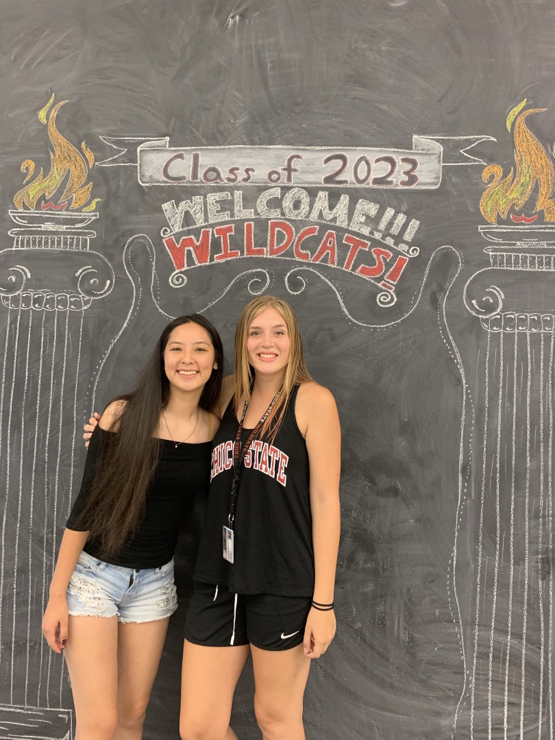 Kate Minderhoud and her roommate Ruby pose in front of a chalkboard that says "Class of 2023 - Welcome Wildcats"