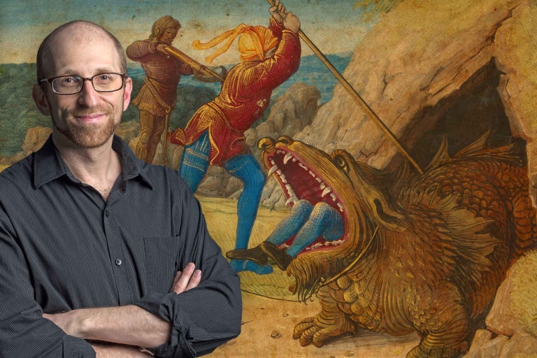 Asa Mittman stands in front of a painting of a monster with a person's feet sticking out of its mouth as humans attempt to stab it.