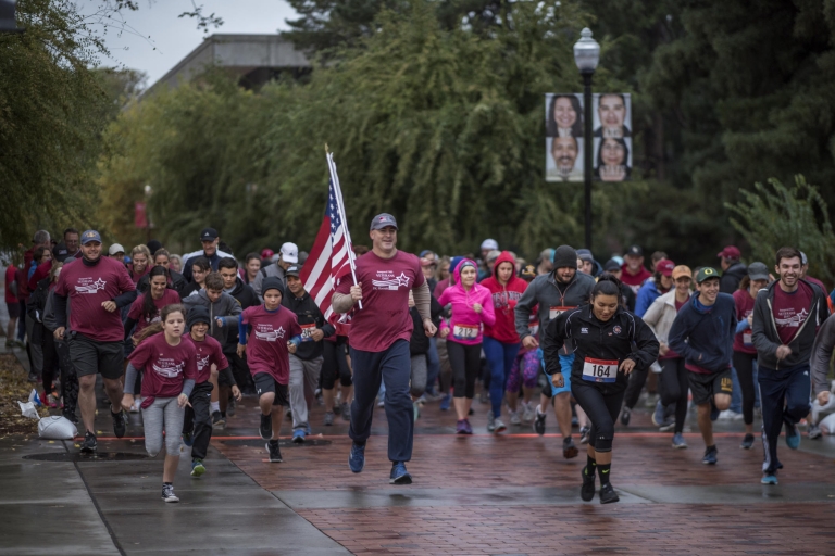 Mike Guzzi runs with the American flag in front of dozens of people, leading them across campus in a 5K run/walk