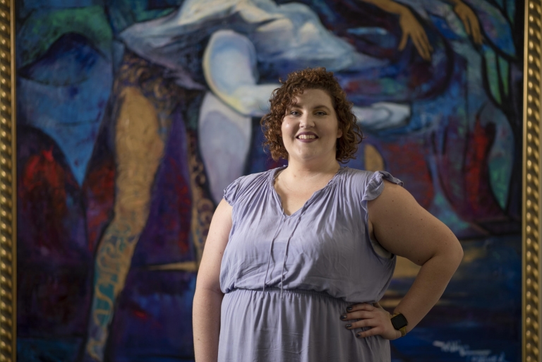 Cory Tondreau smiles as she poses in front of an abstract mural