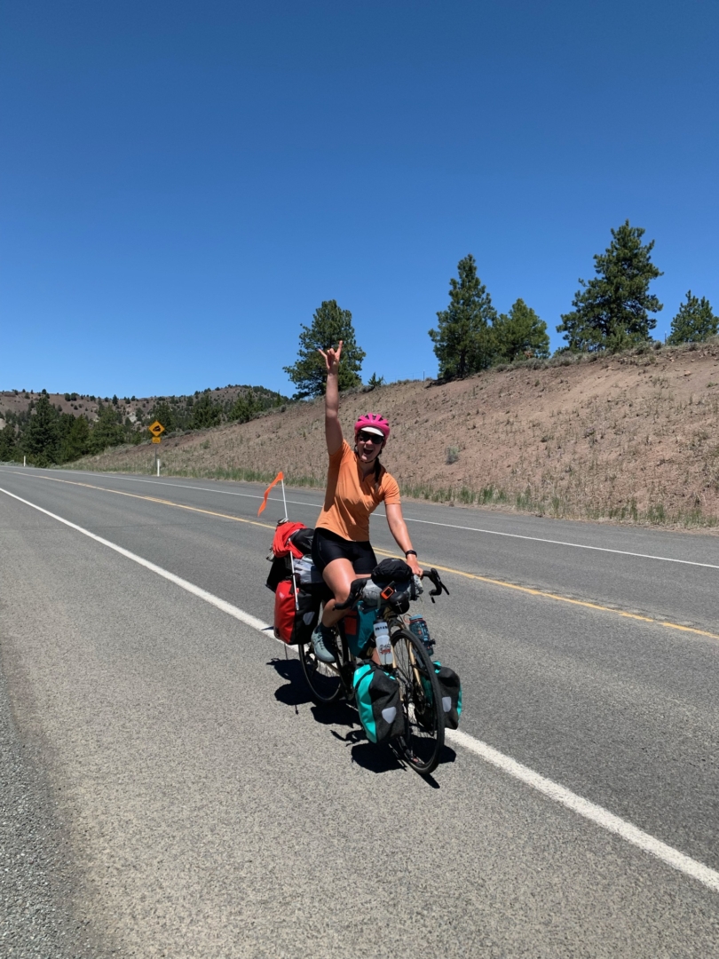 Christine Wilhoyt holds one hand in the air as she descends a hill on her bike.