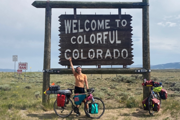Christine Wilhoyt poses with her bike next to a sign welcoming people to Colorado.