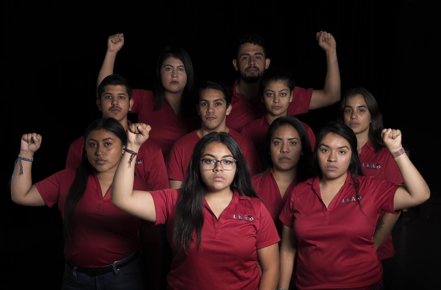 A group of students involved with the Dream Cente raire their fists in show of solidarity and support while all wearing red polos.