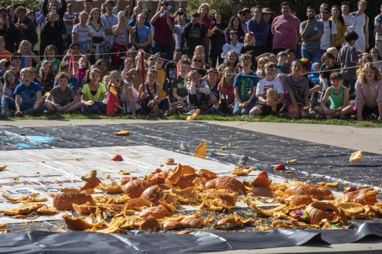 Elementary school students gasp and smile in delight as pumpkins are smashed into a big mess.