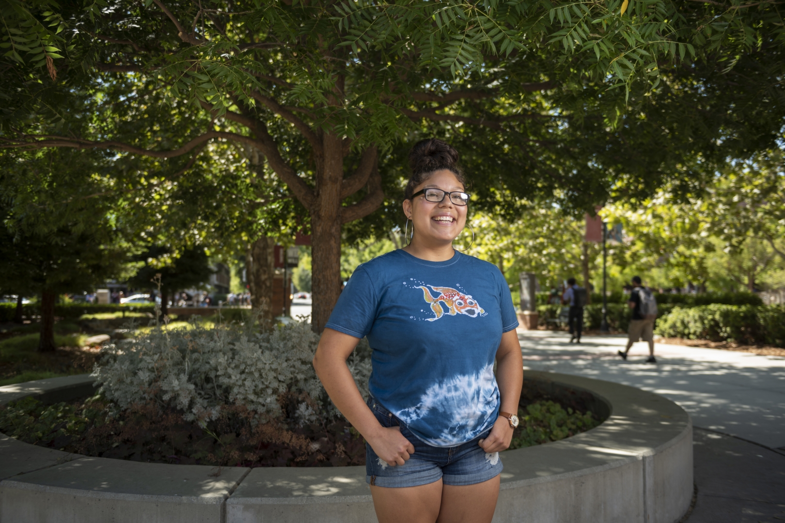 Jacklynn Rodriguez smiles and stands in front of a tree planter box on campus