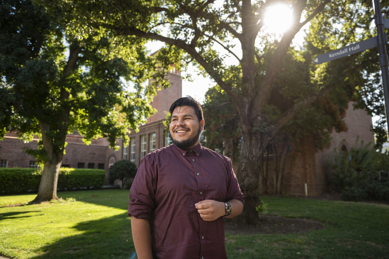 Gustavo Martir smiles in front of Trinity Hall with the sun shining through the trees in the background