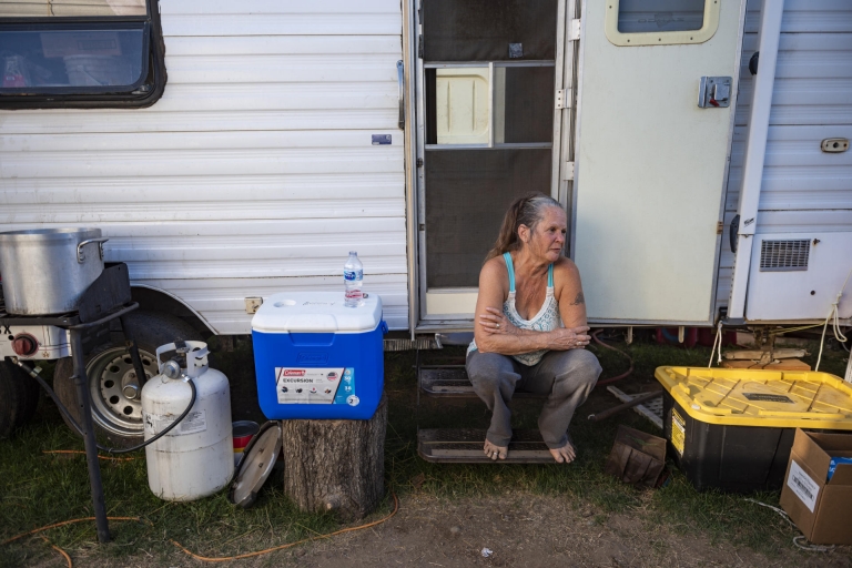 A woman sits on the outdoor step of her travel trailer.