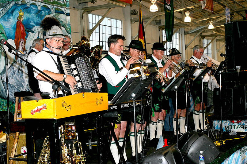 A group of musicians play a variety of instruments on stage while dressed in traditional German clothing.