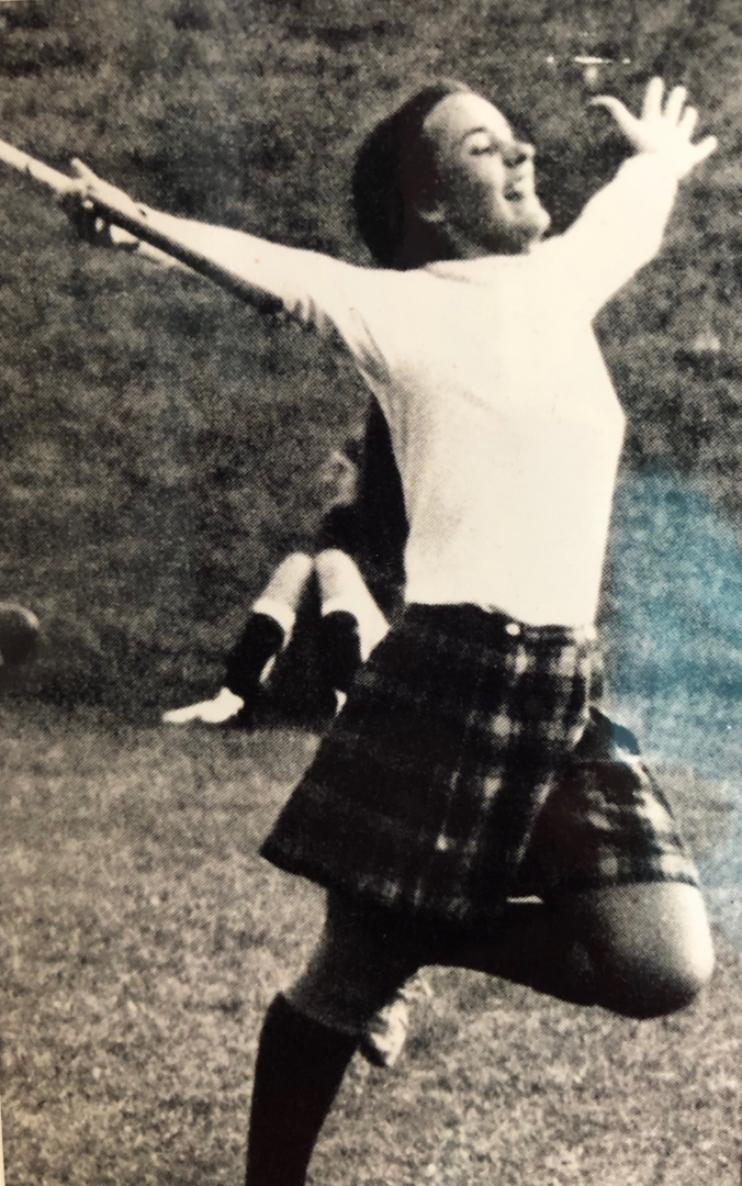 President Hutchinson runs through a field, arms outstretched, wearing a plaid skirt, in this black and white photo.