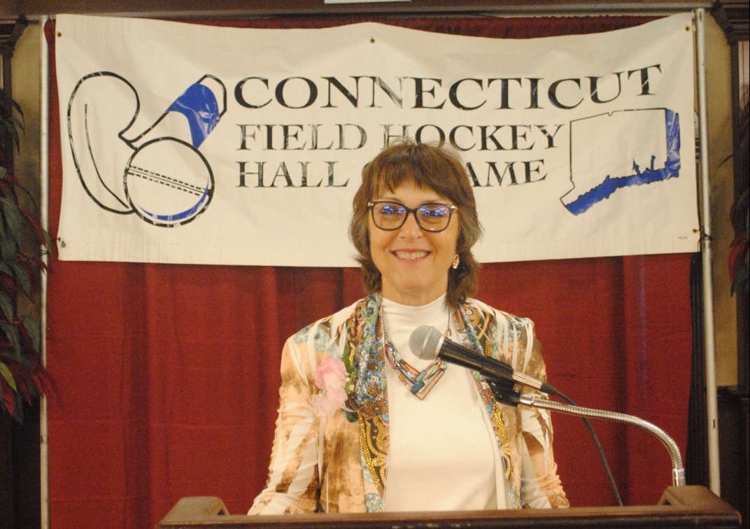 President Hutchinson stands at a podium below a Connecticut Field Hockey Hall of Fame banner.