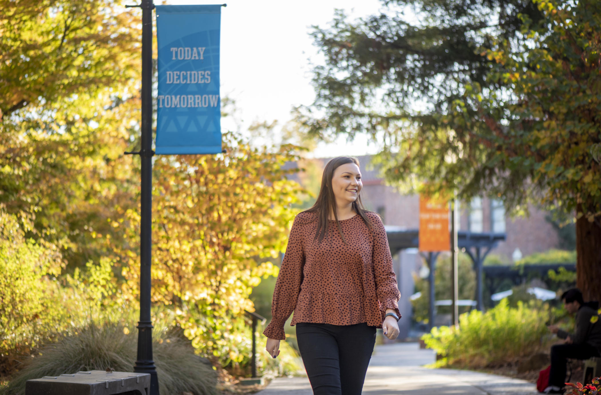 Kelsea Kennedy walks down a path on campus near a pole banner that reads "Today Decides Tomorrow"