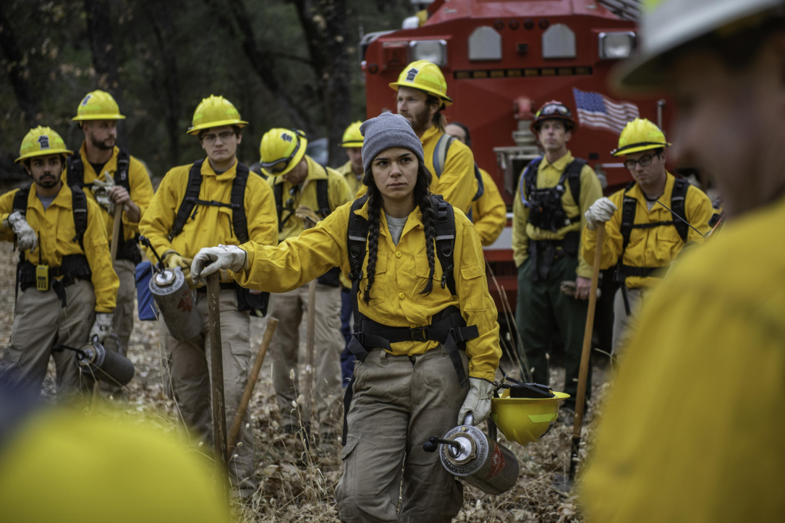 A group of college students wearing fire gear gather in a group and receive instructions.