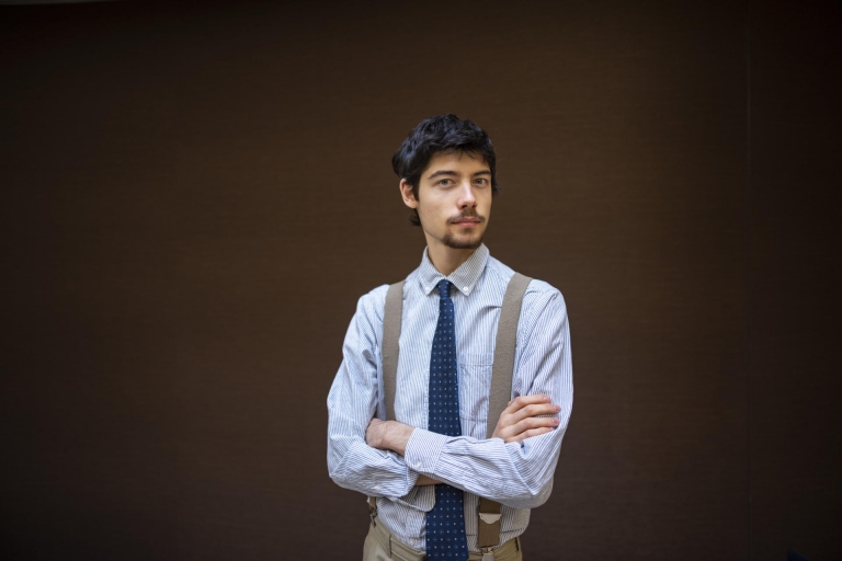 A college student wearing a tie poses in front of a wall.