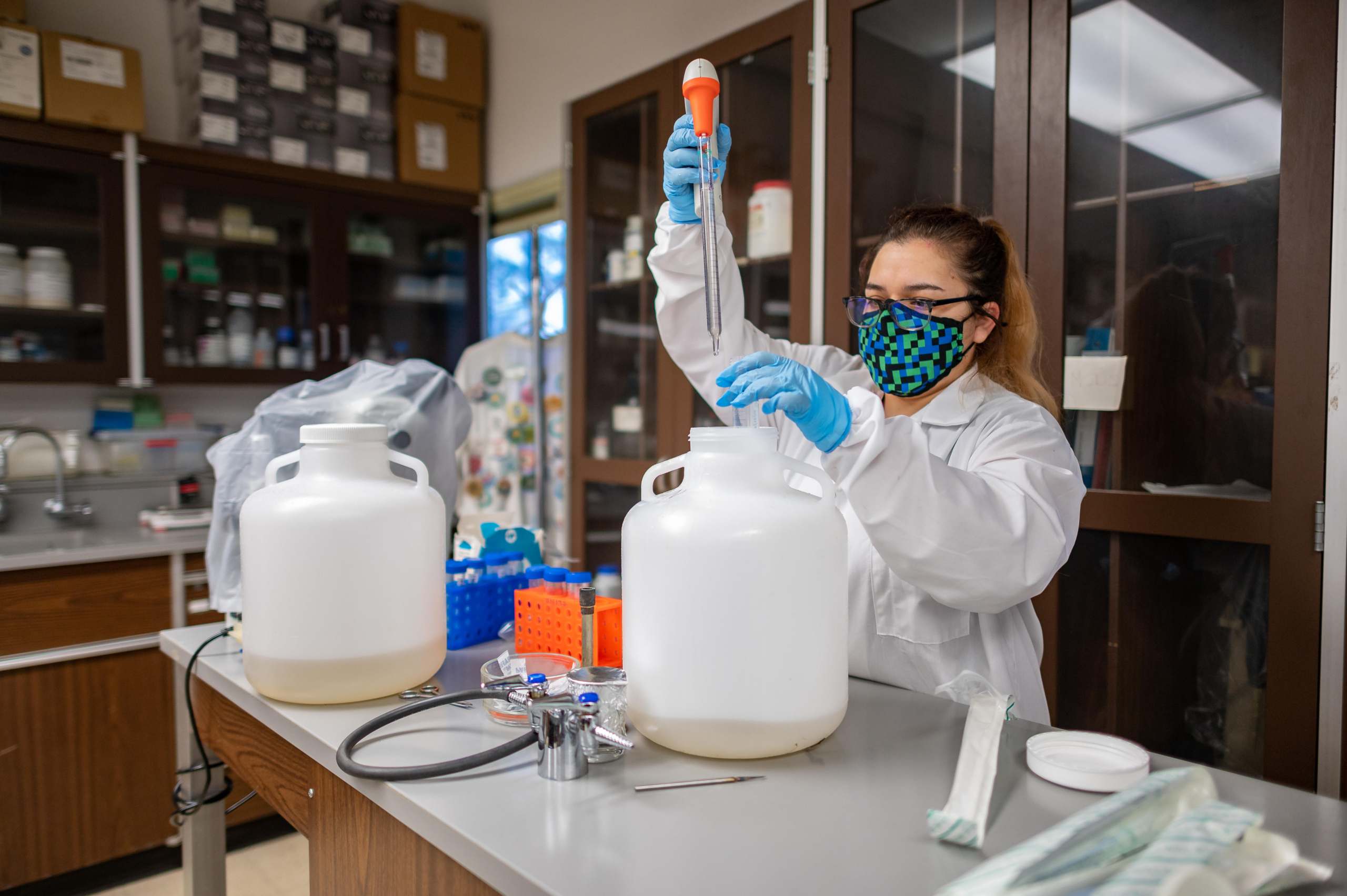 A student pulls a sample of wastewater from a large jug.