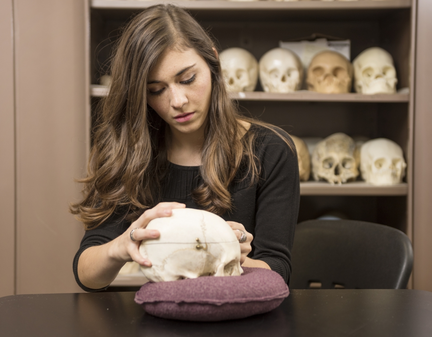 Martha Diaz holds a skull in her hands with a closet of skulls behind her.