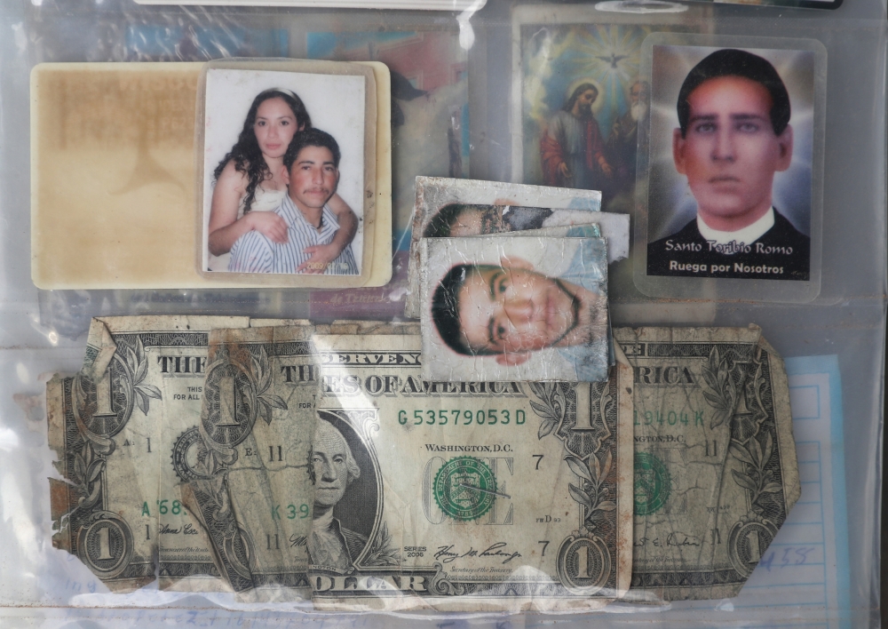 A dollar bill, photographs, and prayer cards sit in plastic sleeves, as evidence found with human remains.