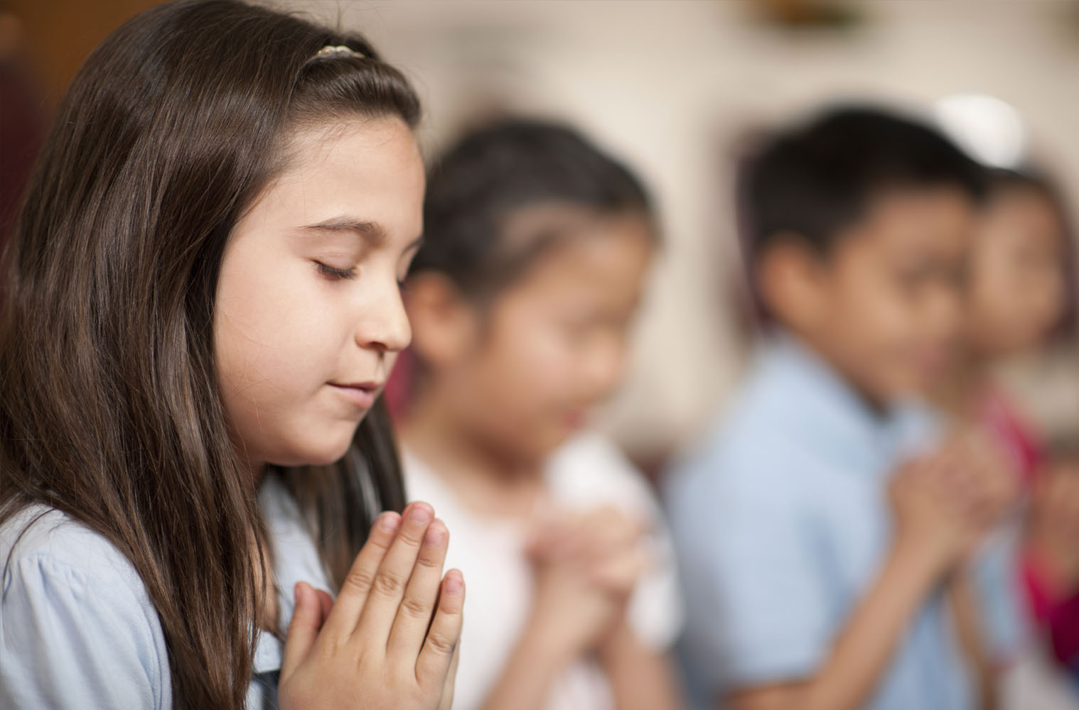 A young girl clasps her hands in prayer with her eyes closed.