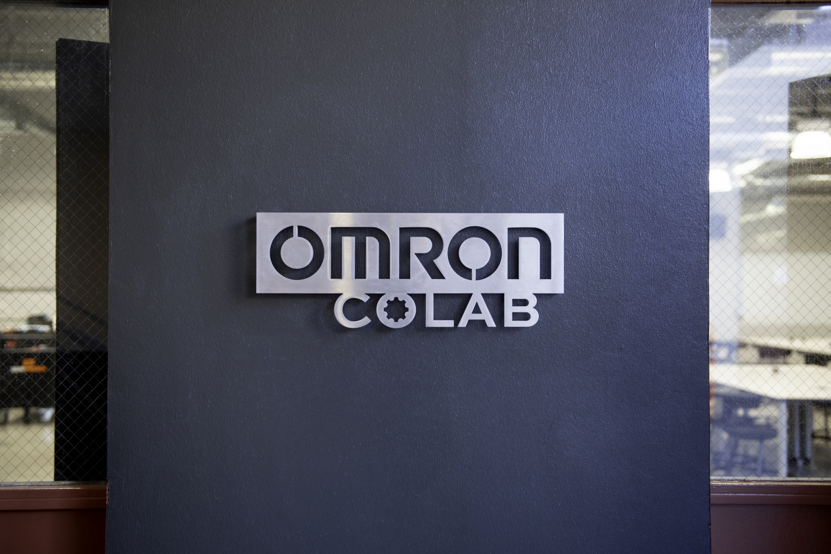 A metal sign saying Omron CoLab hangs on a wall.