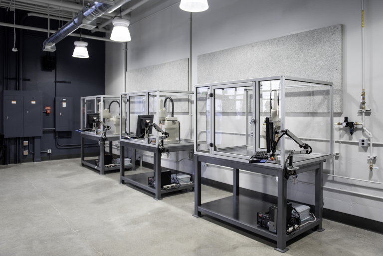 Three industrial robots are lined up inside a room.