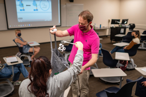 Troy Cline holds a cloth bag out to a student as she "grabs" small white balls with a claw.