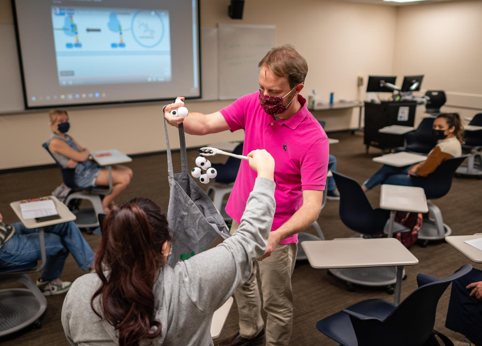 Troy Cline holds a cloth bag out to a student as she "grabs" small white balls with a claw.