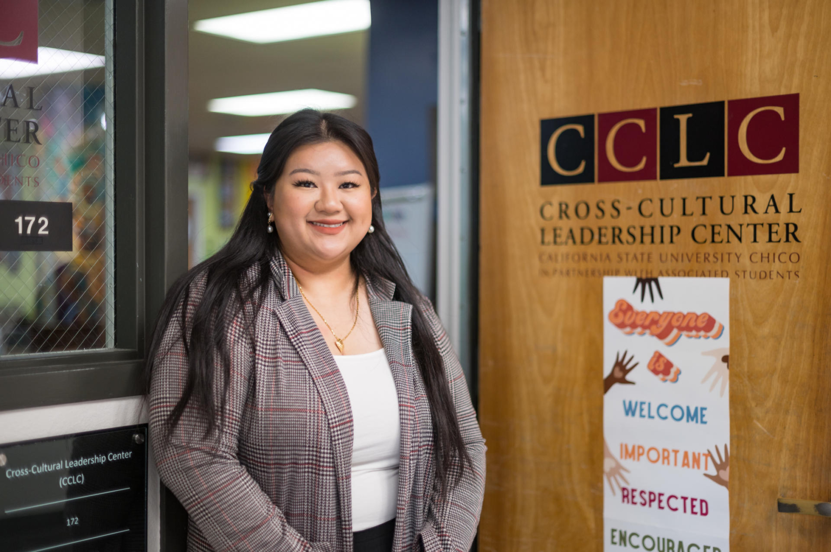Selena Thao poses and smiles standing outside the door of the Cross-Cultural Leadership Center