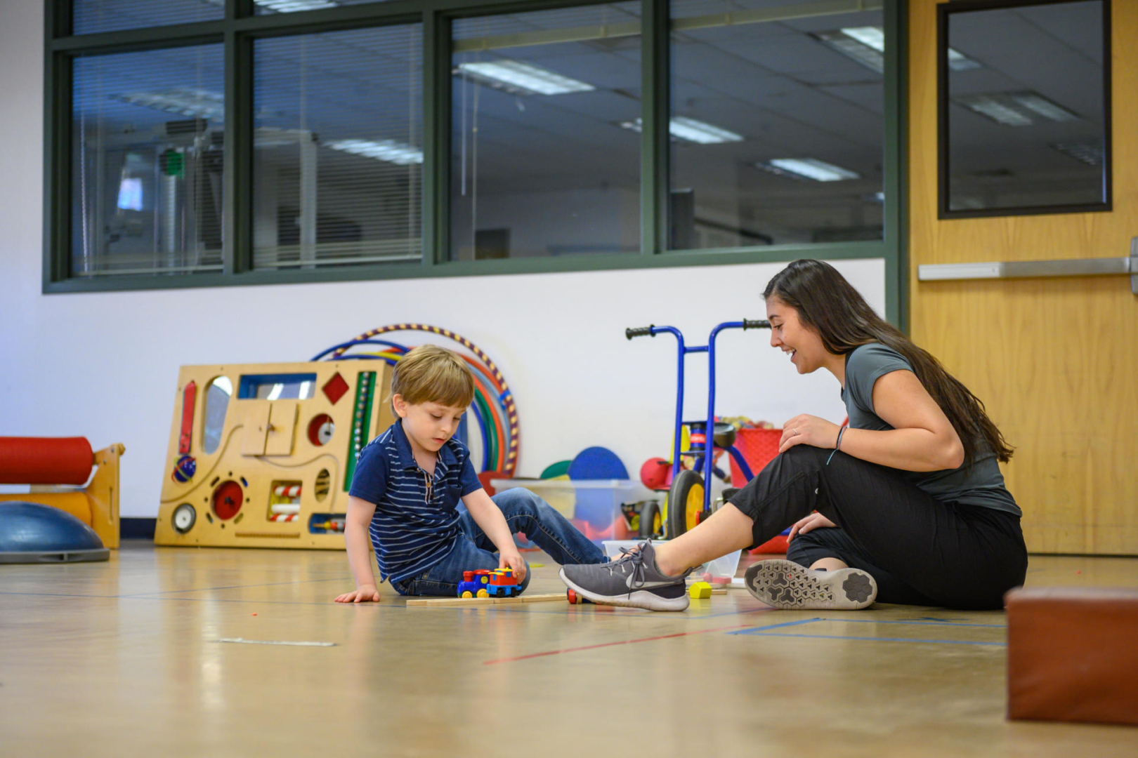 A student and young boy work with small toys on the floor of the autism clinic.