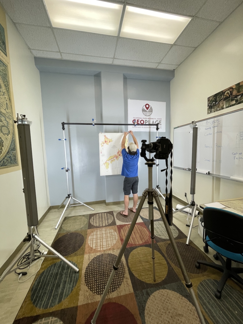 A college student hangs a physical map in front of a camera to take a digital picture