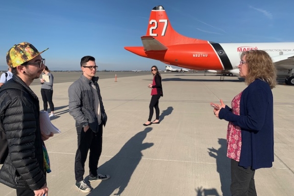 students talk with the airport manager on the tarmac of the airport with a plane in the background.