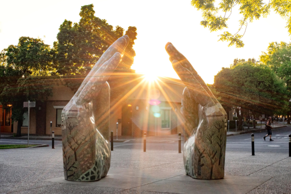 The sun shines through the oversized statue of two hands near the Chico City Hall buildling.