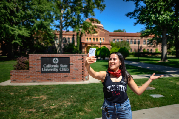 Diana Castellanos gives a virtual campus tour, holding out her self-phone while filming herself in front of the California State University, Chico monument sign.