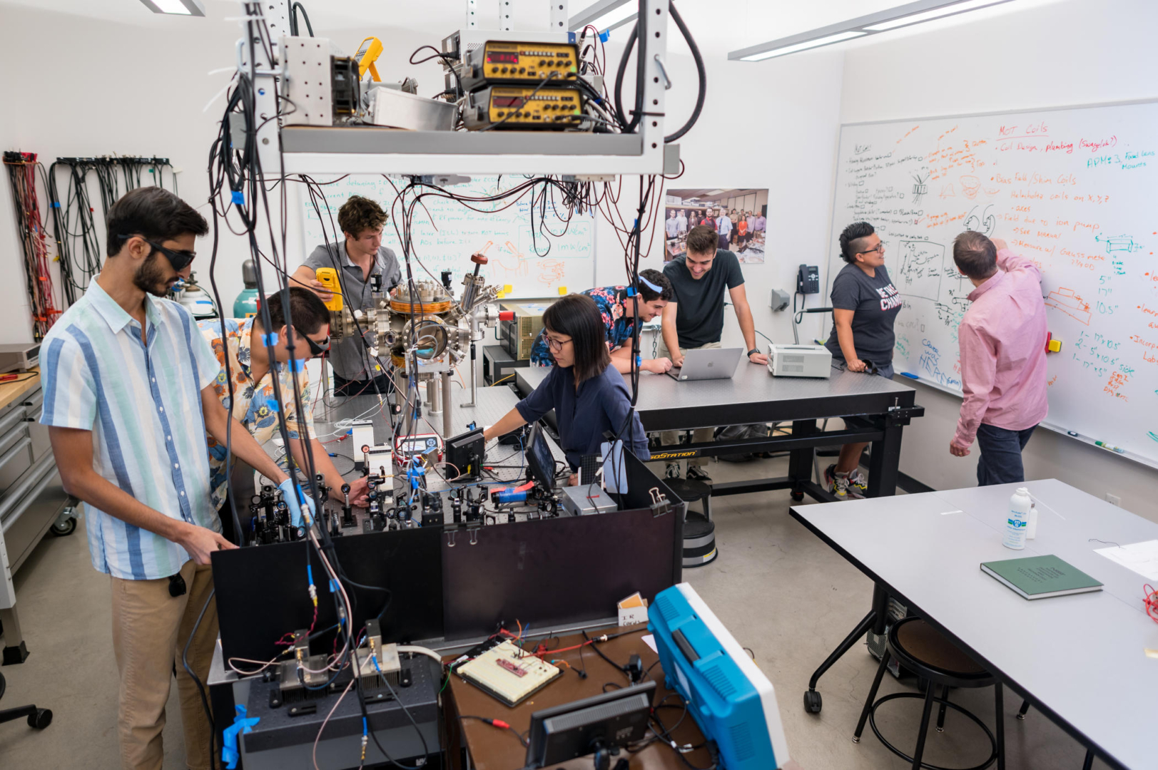 Students and faculty work the ultracold atom laboratory—some working on laptops, others looking at notes on a whiteboard, and others with the lasers and ultrahigh vacuum chamber.