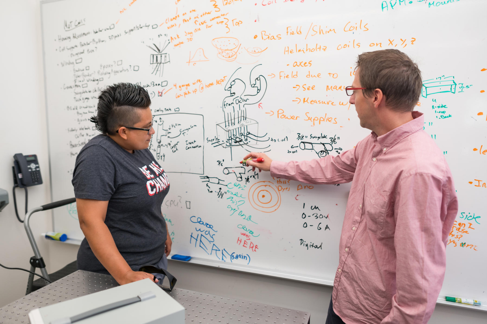 Yolanda Reyes and Joe Pechkis make notes on a whiteboard covered in sketches, equations, and phrases.
