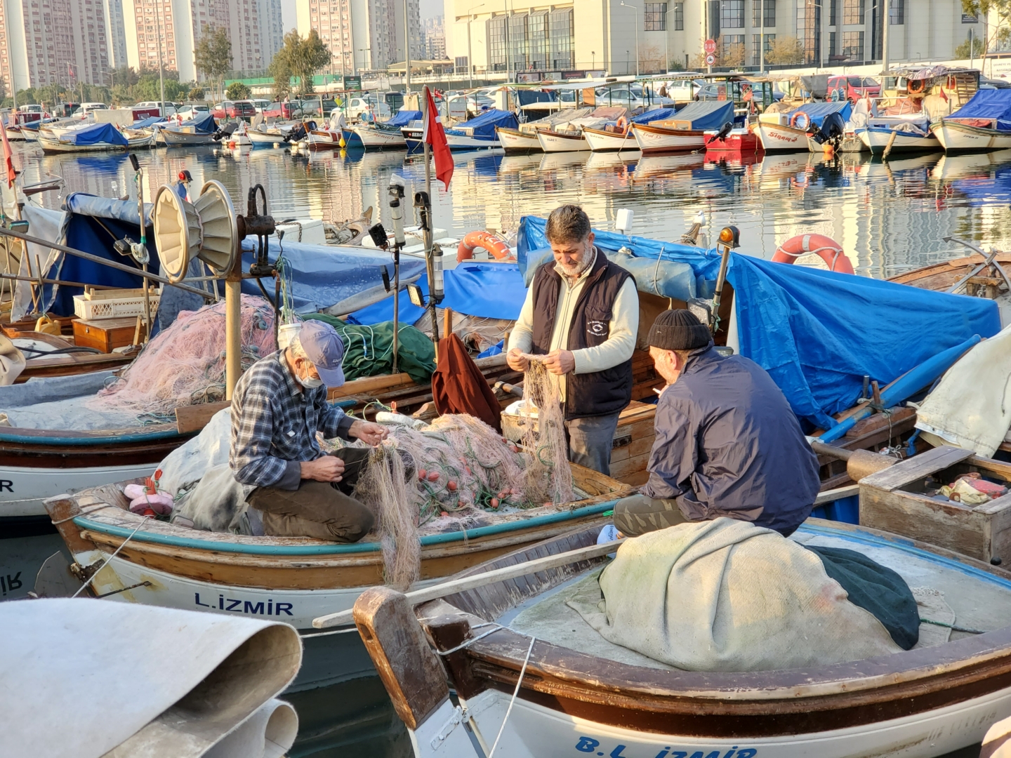 A group of fishermen tie their lines while they sit on boats in a harbor filled with many other fishing boats
