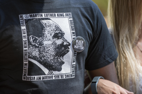 A person wearing a Martin Luther King Jr t-shirt and a Black Lives Matter pin locks arms with another person.