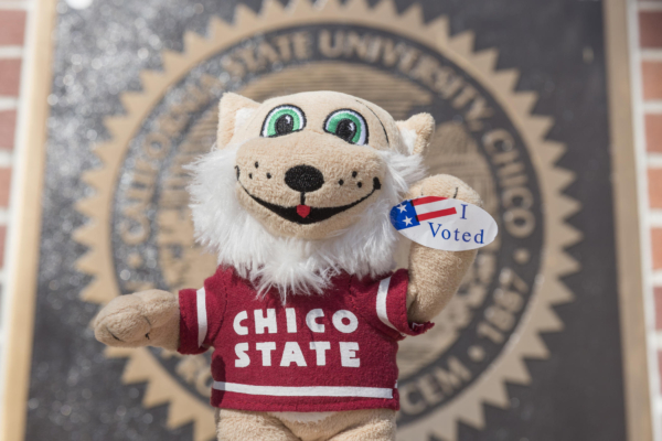 A plush Willie the Wildcat holds out an "I Voted" sticker in front of the university seal.