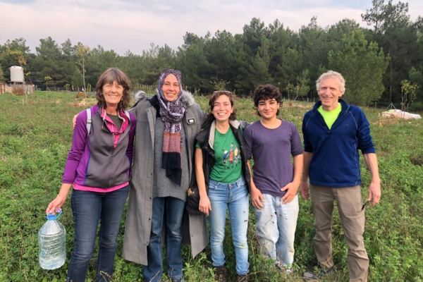 A college faculty and his students pose and smile standing in a lush green field.