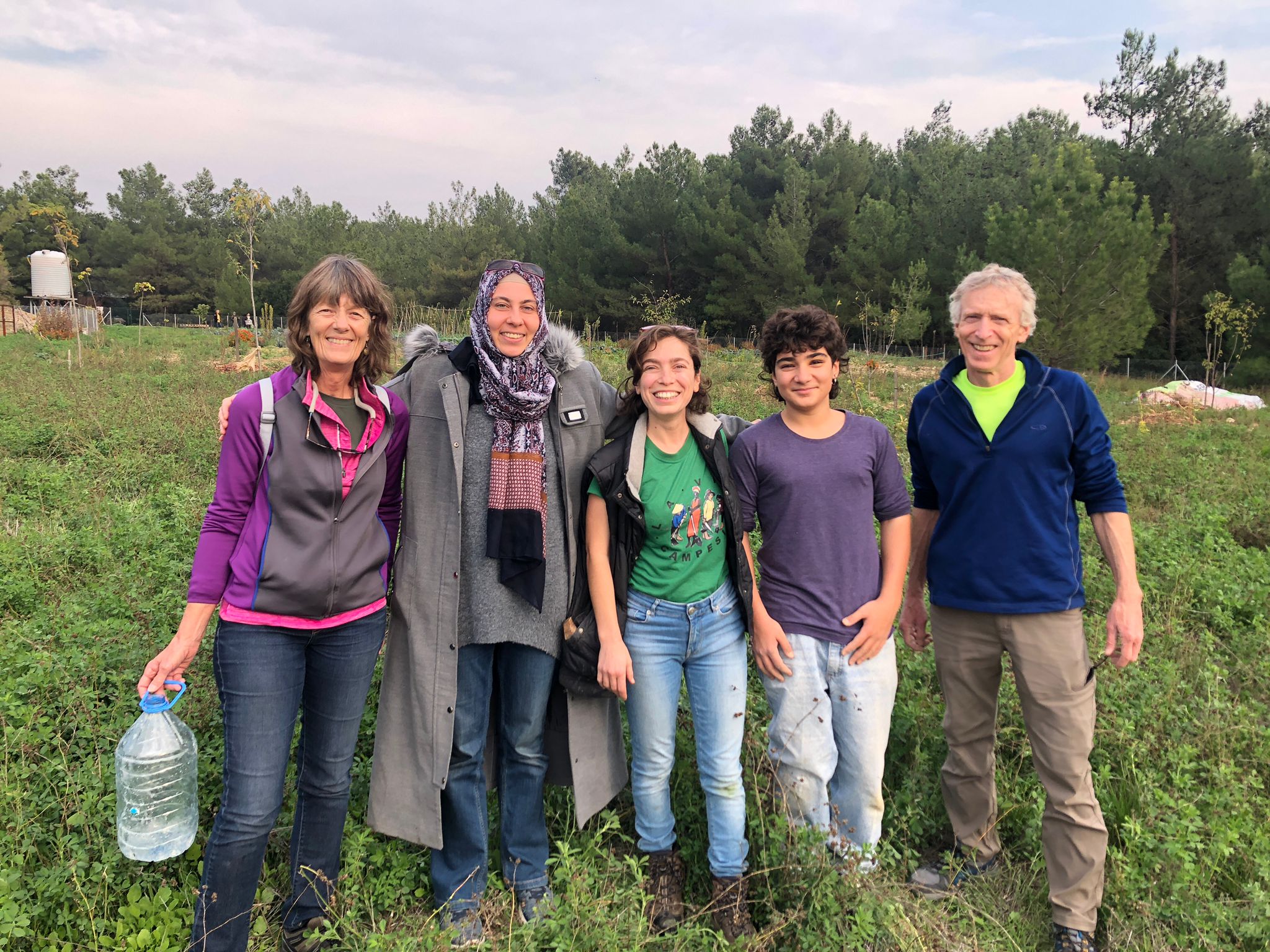 A college faculty and his students pose and smile standing in a lush green field.