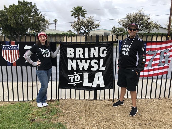 Mark and Lindsay Rojas stand with a "Bring NWSL to LA" flag