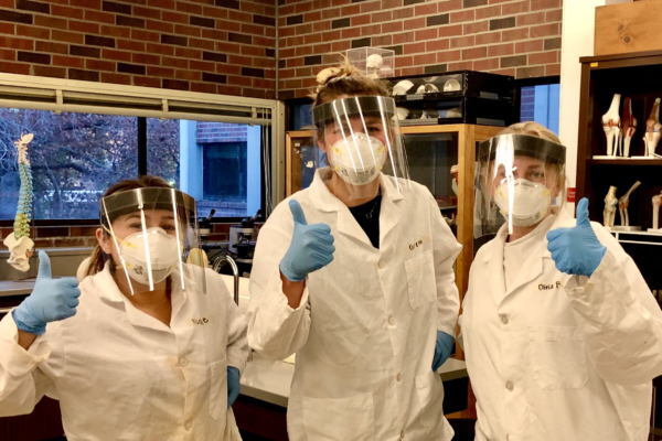 Gretta Kirkby and two of her fellow interns pose in gloves, lab coats, masks, and face shields.