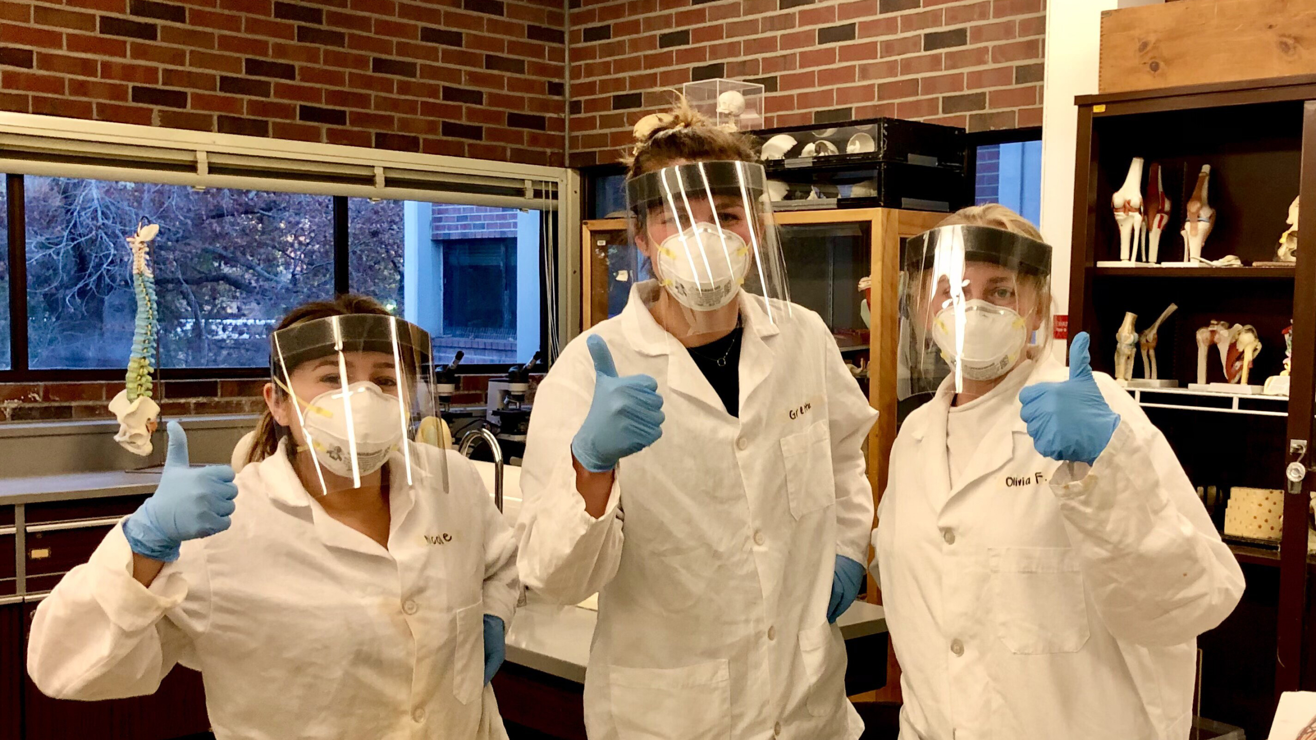 Gretta Kirkby and two of her fellow interns pose in gloves, lab coats, masks, and face shields.