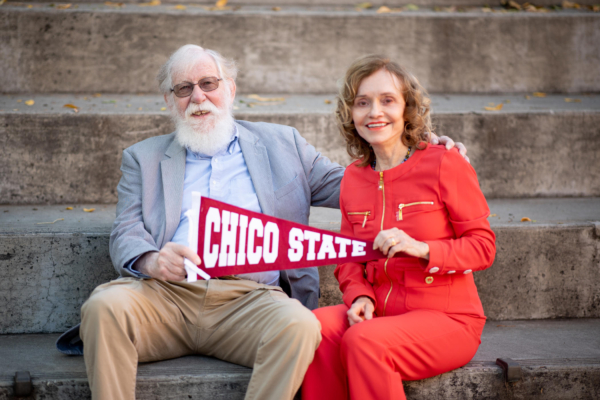 Jon Ebeling and Freddie Shockley sit on some stairs holding a Chico State pennant.