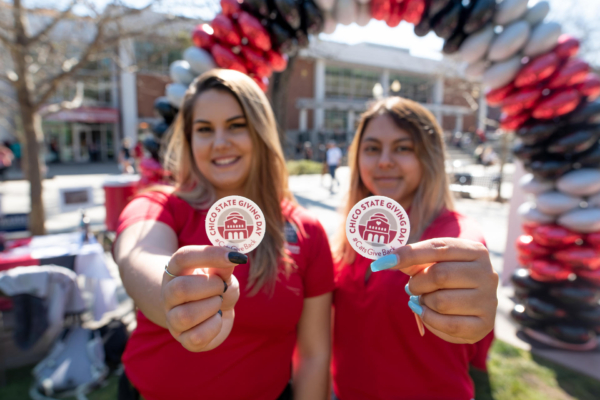 Two female college students standing outside hold stickers for Giving Day.