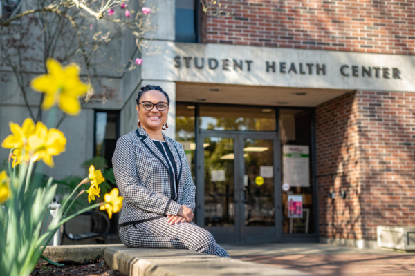 Juanita Mottley sits on a concrete bench with flowers to her right and in front of the Student Health Center