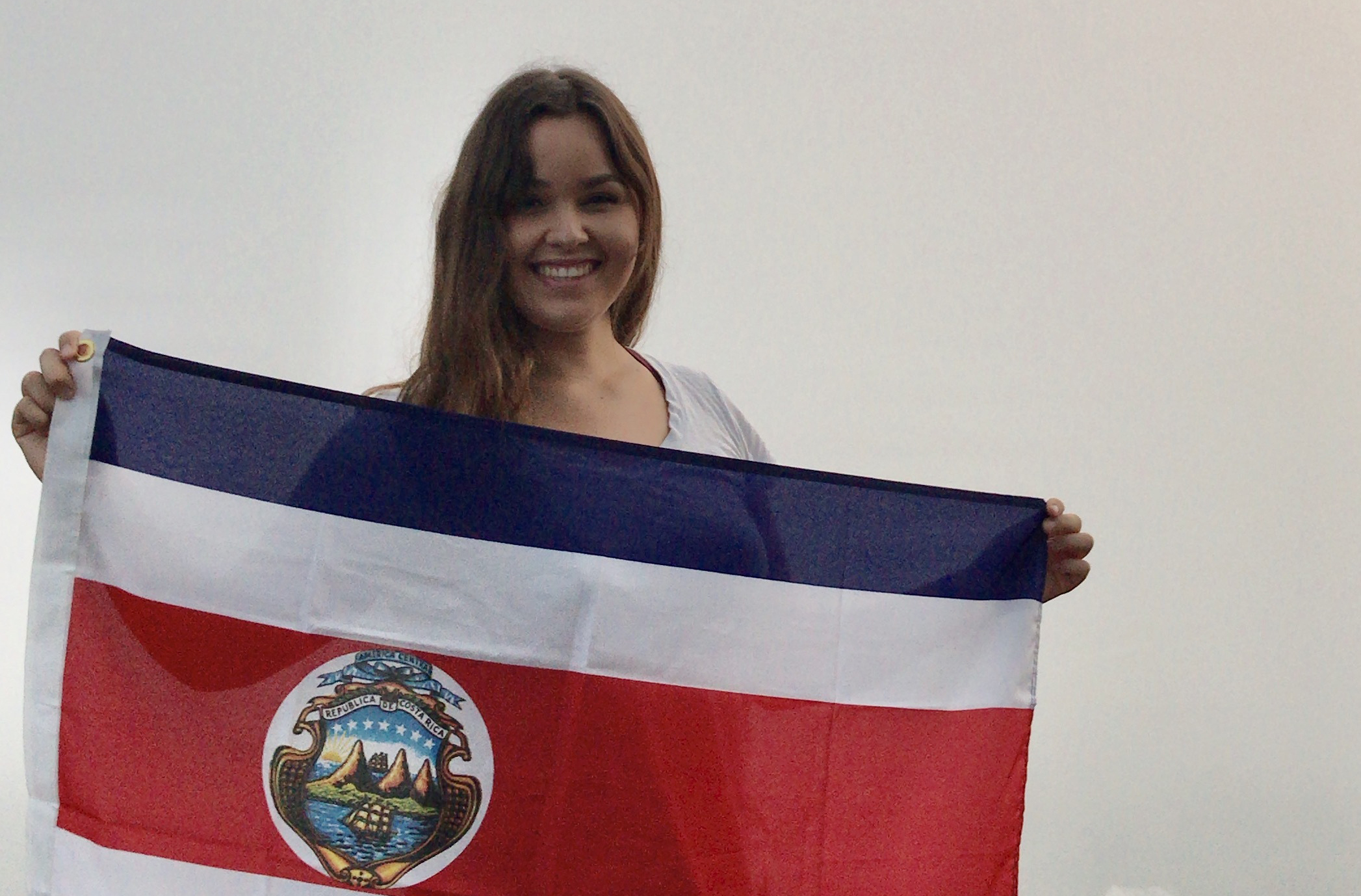 A college student smiles while holding a country's flag.