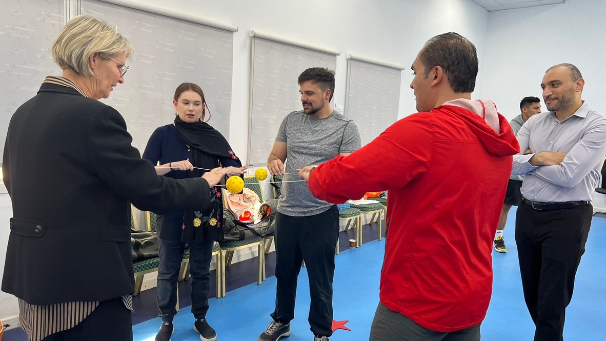 Educators and students interact with educators from the UAE on adapted physical education activities using string and whiffle balls.