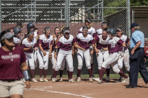 A team of college softball players line up and cheer for a teammate as she prepares to touch home plate.