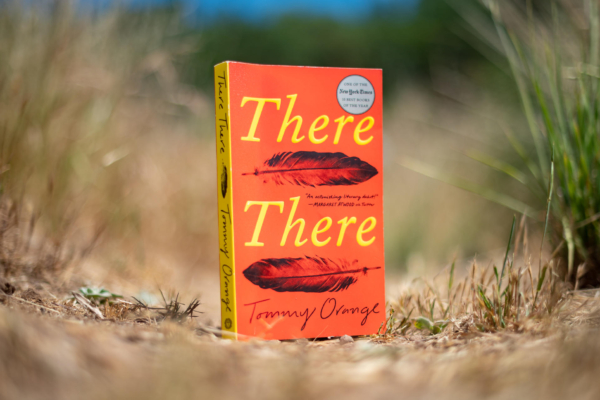 A book titled "There There" sits among a field of grass.