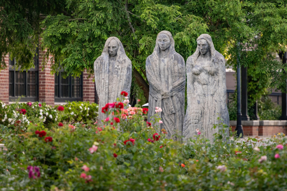 Three stone statues stand amongst rose bushes